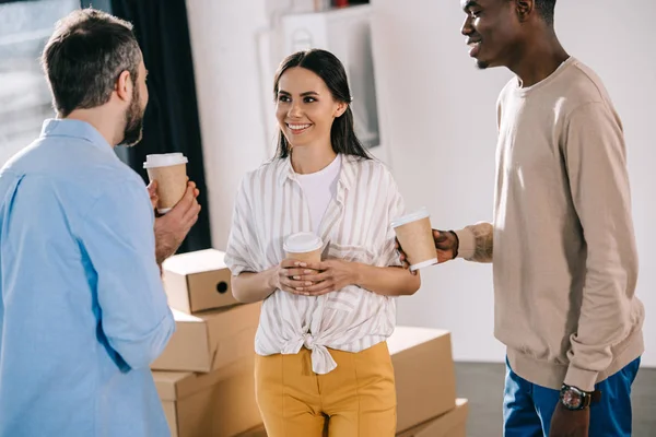 Multiethnische Geschäftskollegen halten Pappbecher in der Hand und unterhalten sich, während sie in ihr neues Büro ziehen — Stockfoto