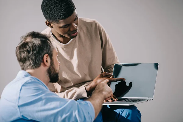 Hombres multiétnicos mirando a la computadora portátil con pantalla en blanco - foto de stock