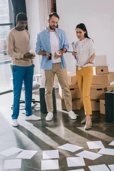 Collègues d'affaires multiethniques debout ensemble et à la recherche de documents dans un nouveau bureau — Photo de stock