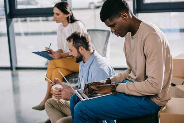 Seitenansicht multiethnischer Geschäftsleute, die im neuen Büro mit digitalen Geräten und Klemmbrett arbeiten — Stockfoto