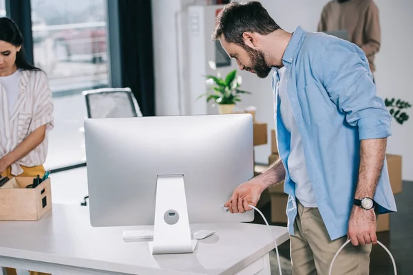 Man holding plug from desktop computer while relocating with coworkers in new office — Stock Photo