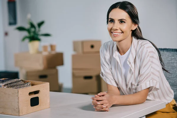 Heureuse jeune femme d'affaires regardant loin tout en étant assis sur le lieu de travail dans un nouveau bureau — Photo de stock