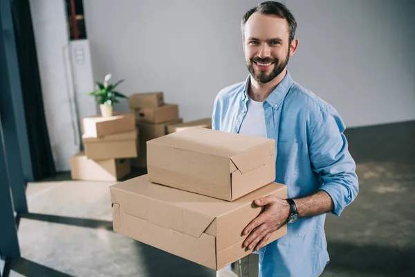 Hombre barbudo feliz sosteniendo cajas y sonriendo a la cámara durante la reubicación - foto de stock