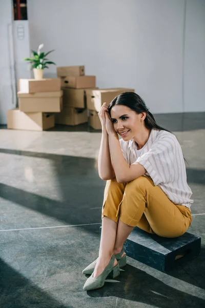 Happy young woman looking away while sitting in new office during relocation — Stock Photo