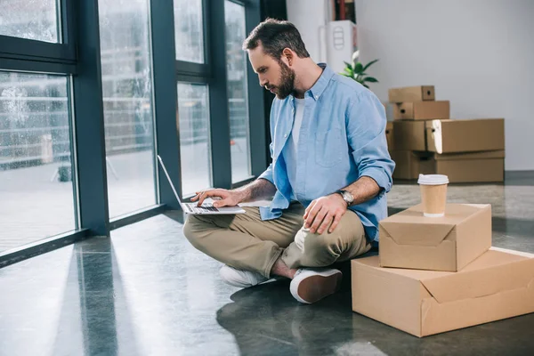 Bärtiger Geschäftsmann sitzt mit Laptop auf dem Boden in neuem Büro — Stockfoto