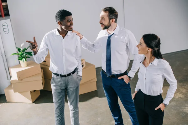 Colegas de negocios multiétnicos felices hablando mientras se mudan a una nueva oficina - foto de stock
