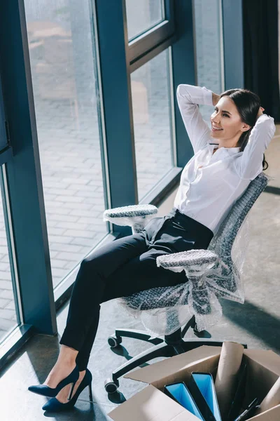 High angle view of happy young businesswoman sitting with hands behind head and looking away in new office — Stock Photo