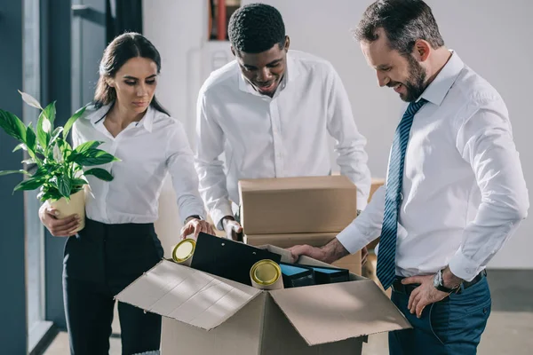 Multiethnische Geschäftsleute in offizieller Kleidung packen in neuem Büro Kartons aus — Stockfoto