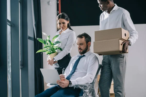 Hommes d'affaires multiethniques avec ordinateur portable, boîtes et plantes en pot déménageant dans un nouveau bureau — Photo de stock