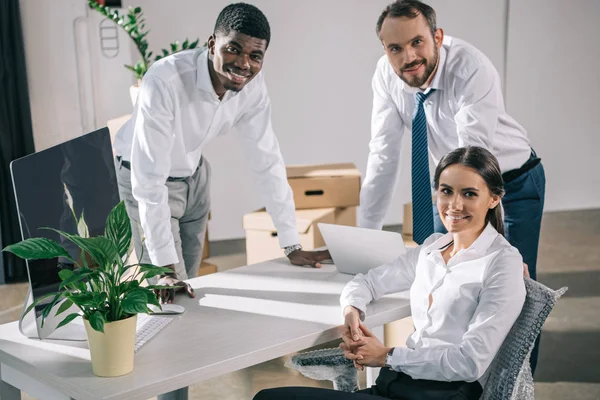 Felices compañeros de trabajo multirraciales sonriendo a la cámara mientras se trasladan a una nueva oficina - foto de stock