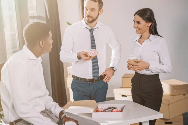 Smiling multiethnic colleagues talking and looking at each other during coffee break in new office — Stock Photo