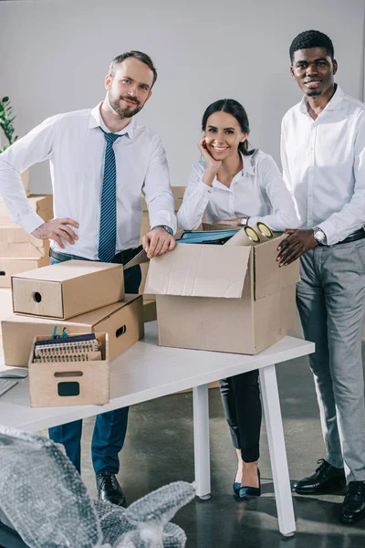 Heureux collaborateurs multiethniques souriant à la caméra et déballer les boîtes dans le nouveau bureau — Photo de stock