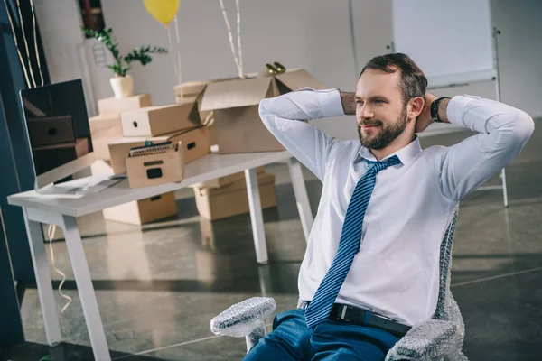 Sonriente hombre de negocios sentado con las manos detrás de la cabeza en una nueva oficina - foto de stock