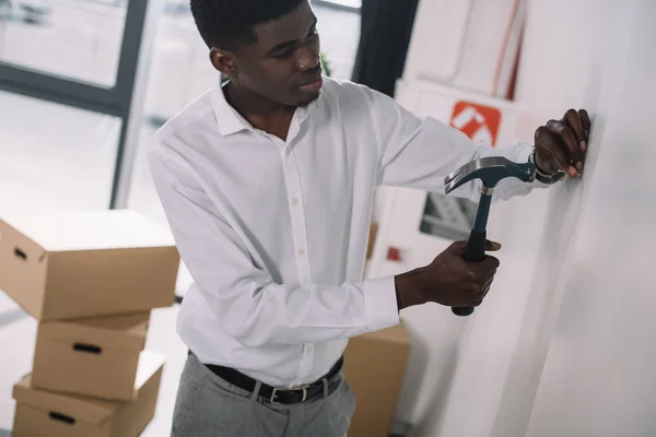 Jovem empresário afro-americano martelando prego em novo escritório — Fotografia de Stock