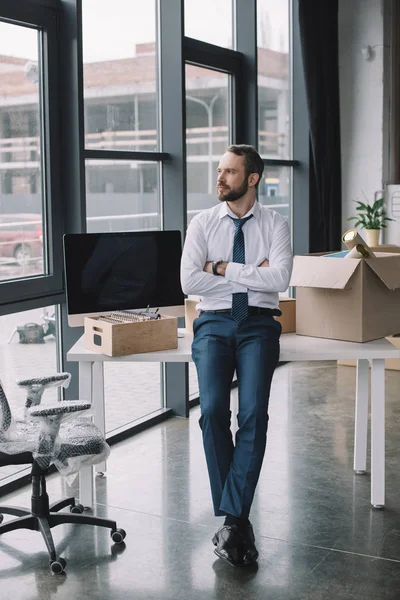 Hombre de negocios con los brazos cruzados sentado en la mesa y mirando hacia otro lado en la nueva oficina - foto de stock