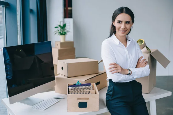 Hermosa joven mujer de negocios con los brazos cruzados sonriendo y mirando hacia otro lado en la nueva oficina - foto de stock