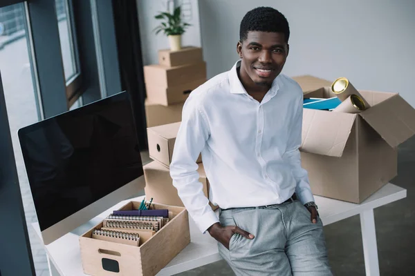 Heureux jeune homme d'affaires afro-américain souriant à la caméra tout en déménageant dans un nouveau bureau — Photo de stock