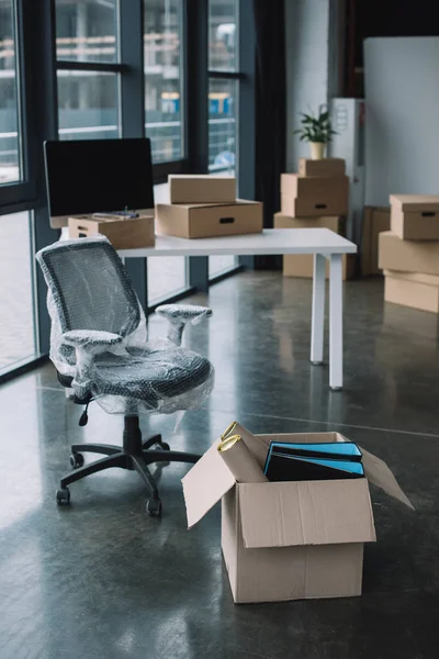 Chaise enveloppée et boîtes en carton dans le bureau lors de la réinstallation — Photo de stock