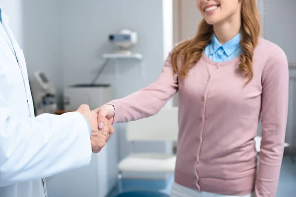 Immagine ritagliata di oftalmologo e paziente sorridente che stringe la mano in clinica — Foto stock