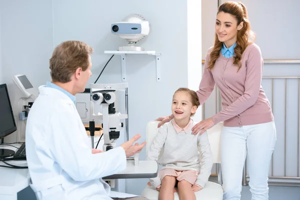 Madre e hija sonriente hablando con el oftalmólogo en la sala de consulta - foto de stock