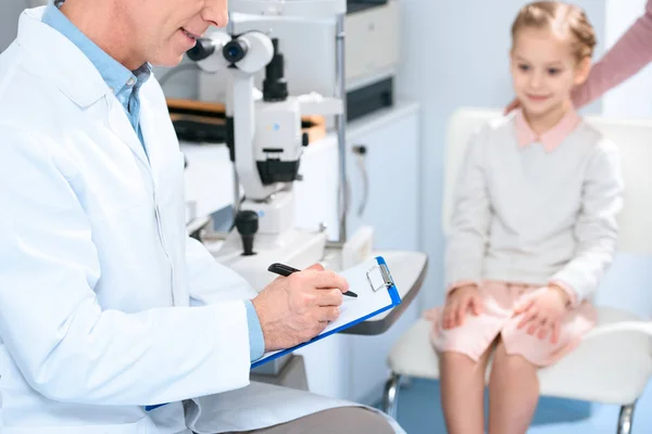 Cropped image of ophthalmologist writing something to patient clipboard — Stock Photo