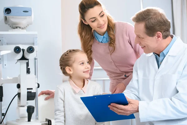 Lächelnder Augenarzt zeigt Patientin etwas im Klemmbrett — Stockfoto