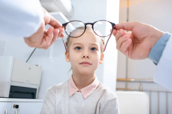 Imagen recortada del oftalmólogo que usa gafas nuevas en el niño preadolescente en la clínica - foto de stock
