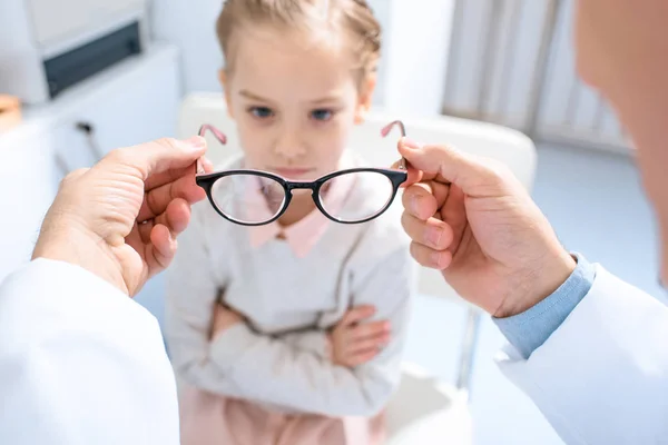 Geschnittenes Bild eines Augenarztes, der unglücklichem Kind in der Klinik eine neue Brille vorschlägt — Stockfoto