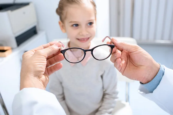 Immagine ritagliata dell'oftalmologo che propone nuovi occhiali al bambino pre-adolescente in clinica — Foto stock