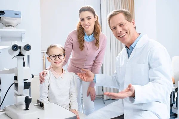 Madre e hija feliz en gafas nuevas mirando a la cámara en la sala de consulta oftalmólogo - foto de stock