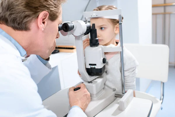 Офтальмолог осматривает зрение ребенка-подростка с щелевой лампой в клинике — стоковое фото