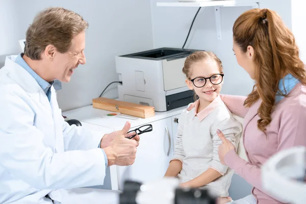 Mother looking at daughter with new glasses in oculist consulting room — Stock Photo