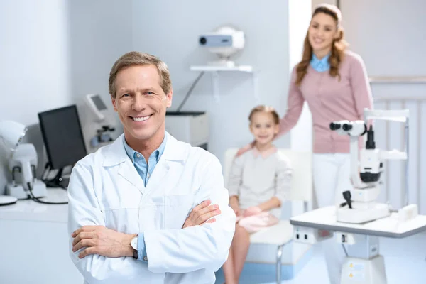 Smiling ophthalmologist and mother with daughter in consulting room — Stock Photo