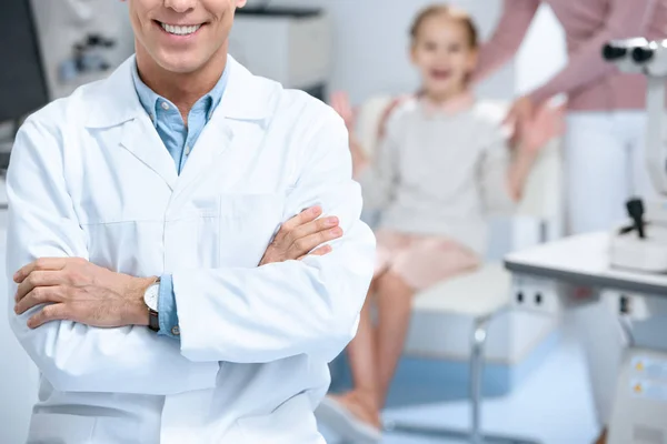 Abgeschnittenes Bild eines lächelnden Augenarztes, der mit verschränkten Armen im Sprechzimmer steht — Stockfoto