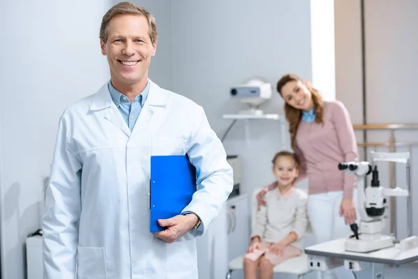 Lächelnder gutaussehender Augenarzt blickt im Sprechzimmer in die Kamera — Stockfoto