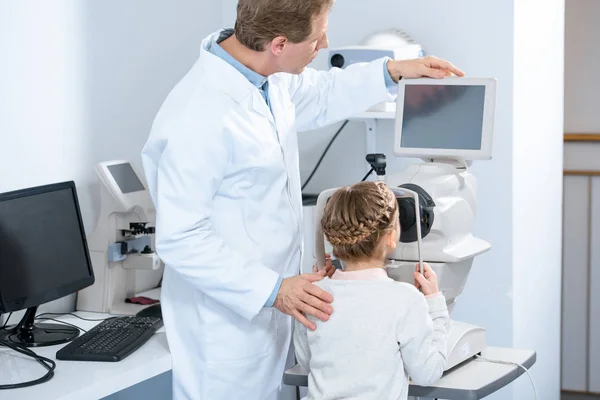 Vista posterior del oftalmólogo que examina la visión del niño preadolescente en la clínica - foto de stock