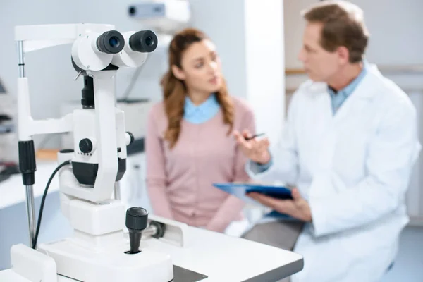 Oculist and patient in clinic with slit lamp on foreground — Stock Photo