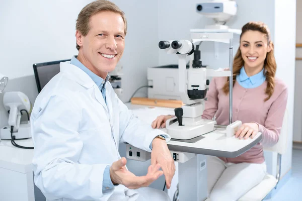 Oftalmólogo sonriente y paciente cerca de lámpara de hendidura en clínica - foto de stock