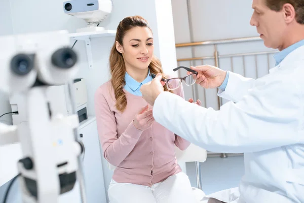 Bello oftalmologo dando occhiali sorridenti paziente in clinica — Foto stock