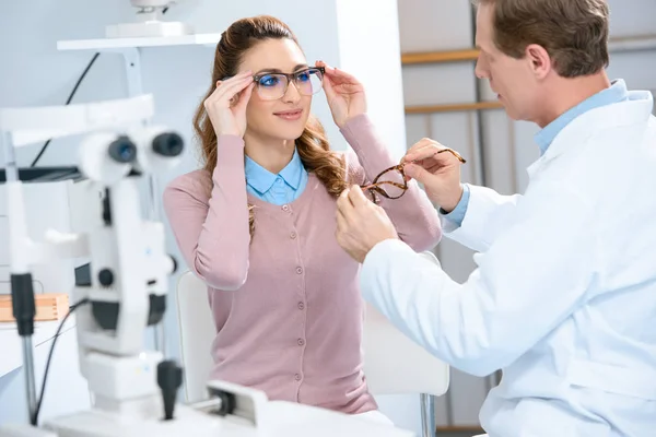 Oftalmólogo ayuda al paciente a elegir gafas con lentes necesarias en la clínica - foto de stock