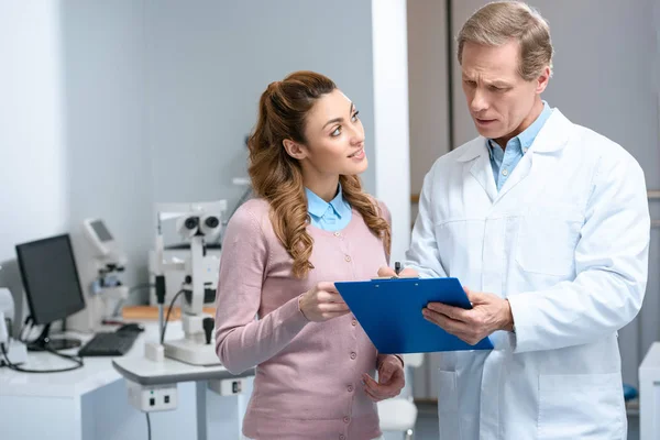 Patient looking at ophthalmologist with clipboard in clinic — Stock Photo