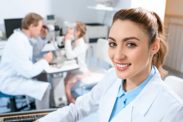 Oftalmologista sorridente segurando lentes para quadro experimental enquanto colega examinando criança com teste de campo visual — Fotografia de Stock