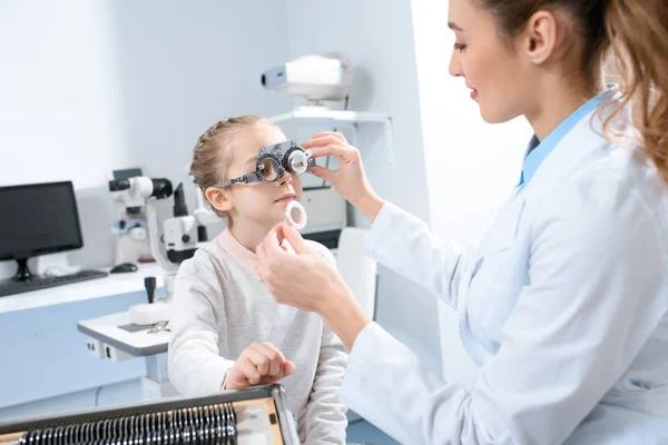 Female ophthalmologist examining kid eyes with trial frame and lenses — Stock Photo