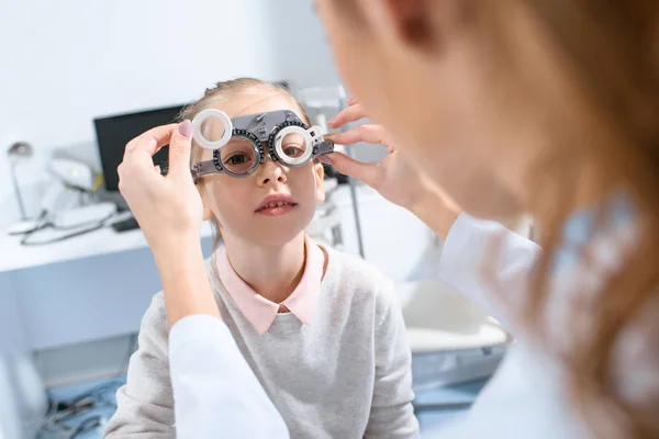 Enfoque selectivo del oftalmólogo que examina los ojos del niño con el marco del ensayo en la clínica - foto de stock