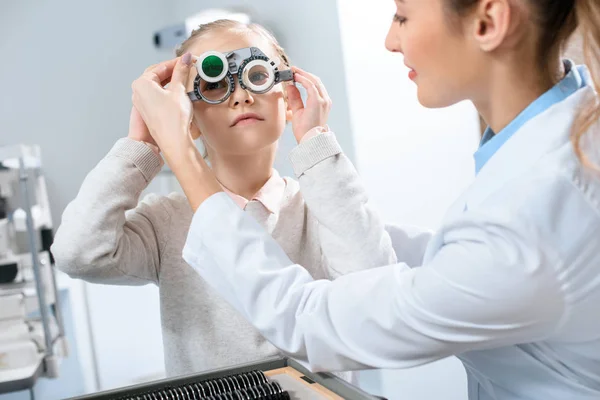 Женщина-окулист осматривает глаза ребенка с пробной рамкой и линзами — стоковое фото