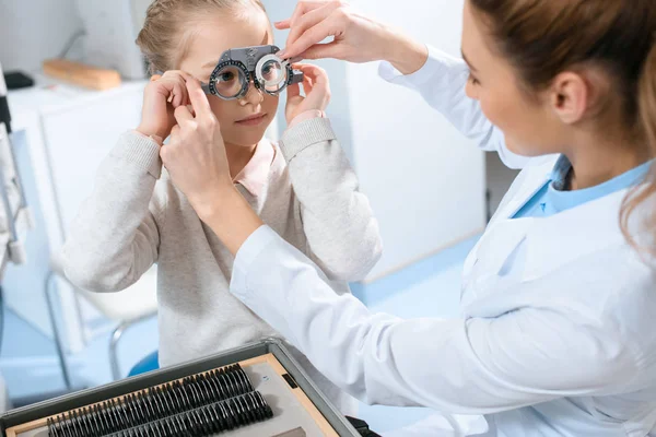 Female ophthalmologist examining kid eyes with trial frame and lenses — Stock Photo