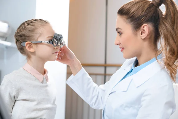 Оптометрист осматривает глаза ребенка с пробной рамкой в клинике — стоковое фото