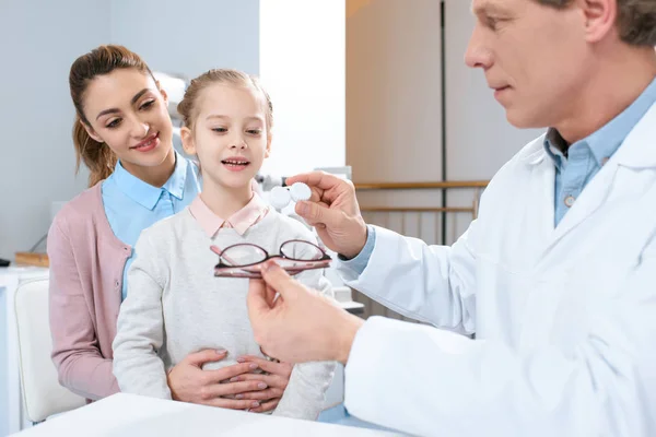 Madre e hija visitando al optometrista y eligiendo anteojos o lentes de contacto en la clínica - foto de stock