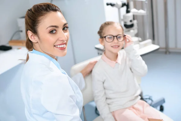 Smiling ophthalmologist and kid in eyeglasses in optics — Stock Photo