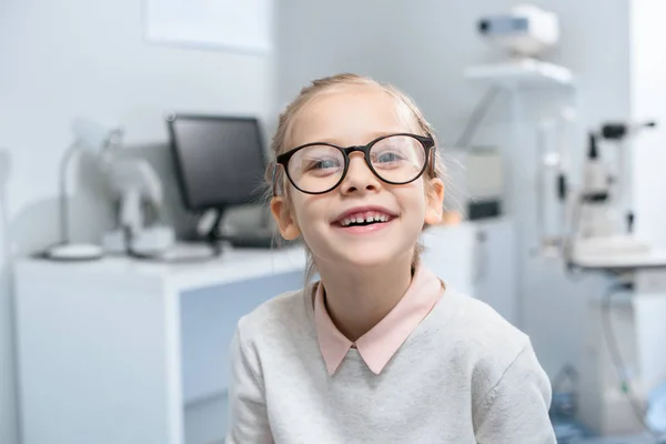 Усміхнена маленька дитина в окулярах у оптичній клініці — стокове фото